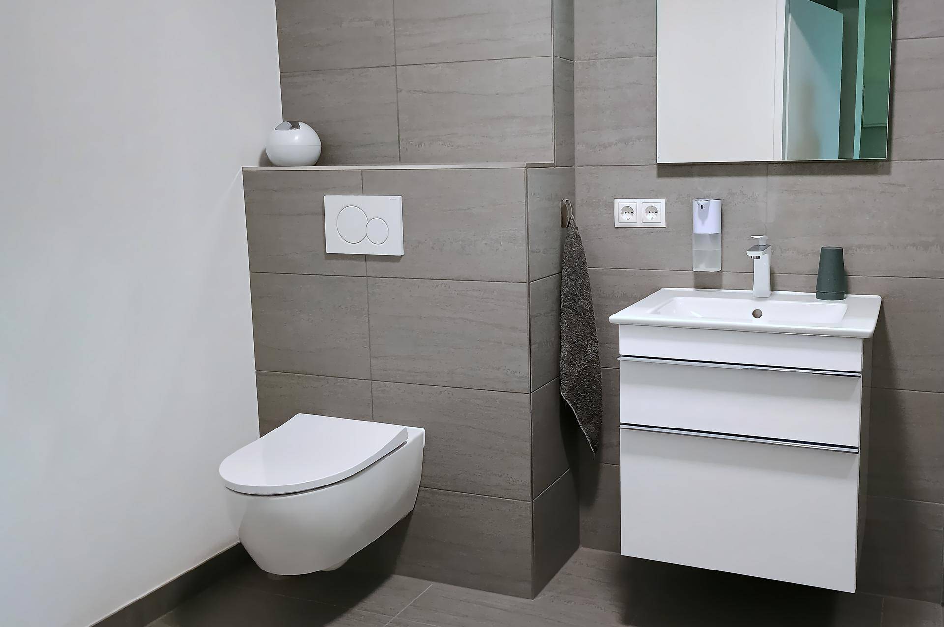 Modernes Gäste-WC mit wandhängender Toilette, Waschbecken und grauen Fliesen.