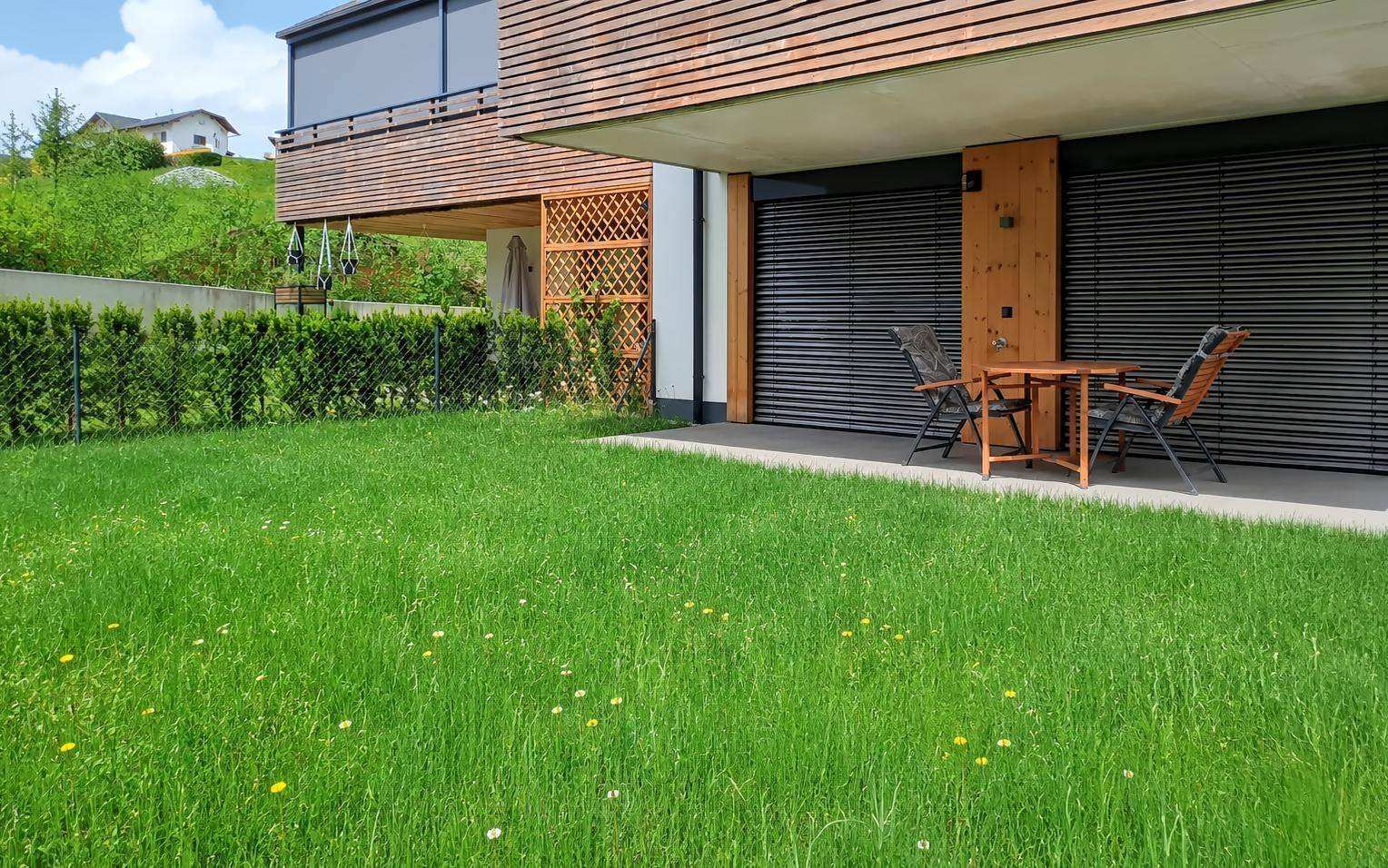 Gepflegter Gartenbereich mit Rasenfläche und kleiner Terrasse vor dem modernen Gebäude.