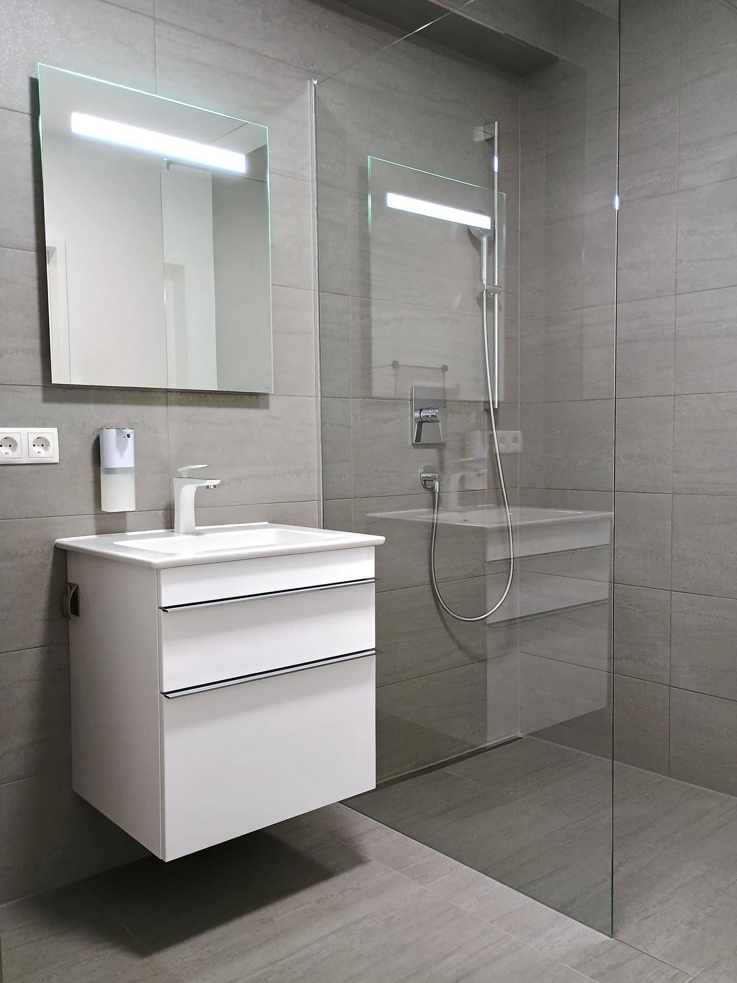 Modernes Badezimmer mit grauen Fliesen, geräumiger Duschkabine und schwebendem Waschtisch.
