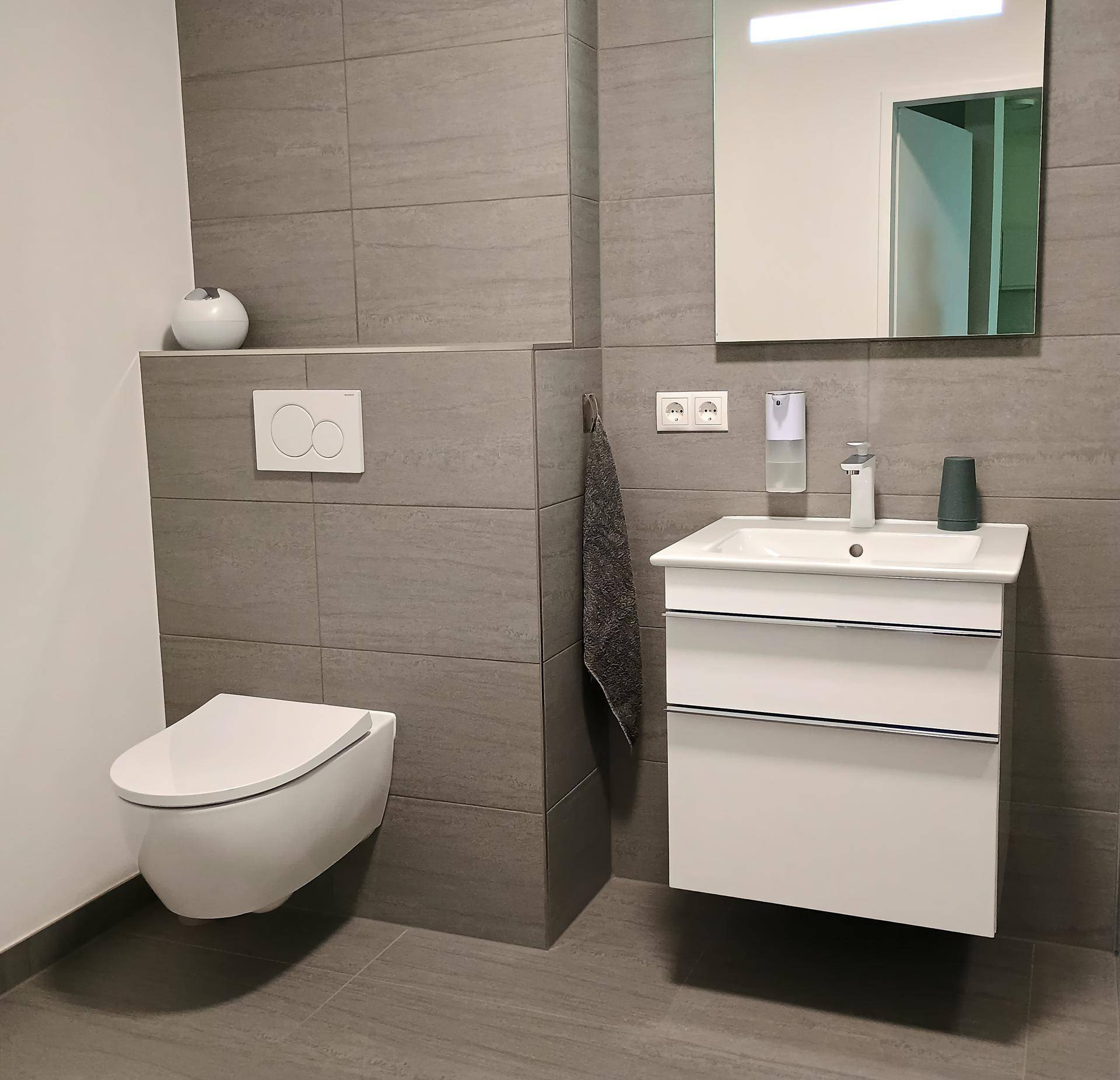 Zeitgemäßes Badezimmer mit grauen Fliesen, wandhängendem WC und praktischem Waschtisch.
