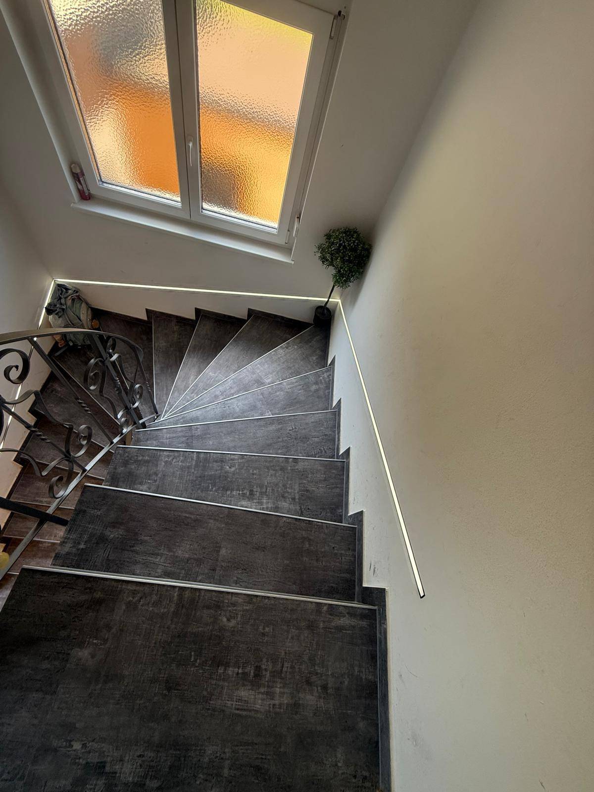 Treppenhaus mit dunklen Stufen, schmiedeeisernem Geländer und Fenster für natürliches Licht.