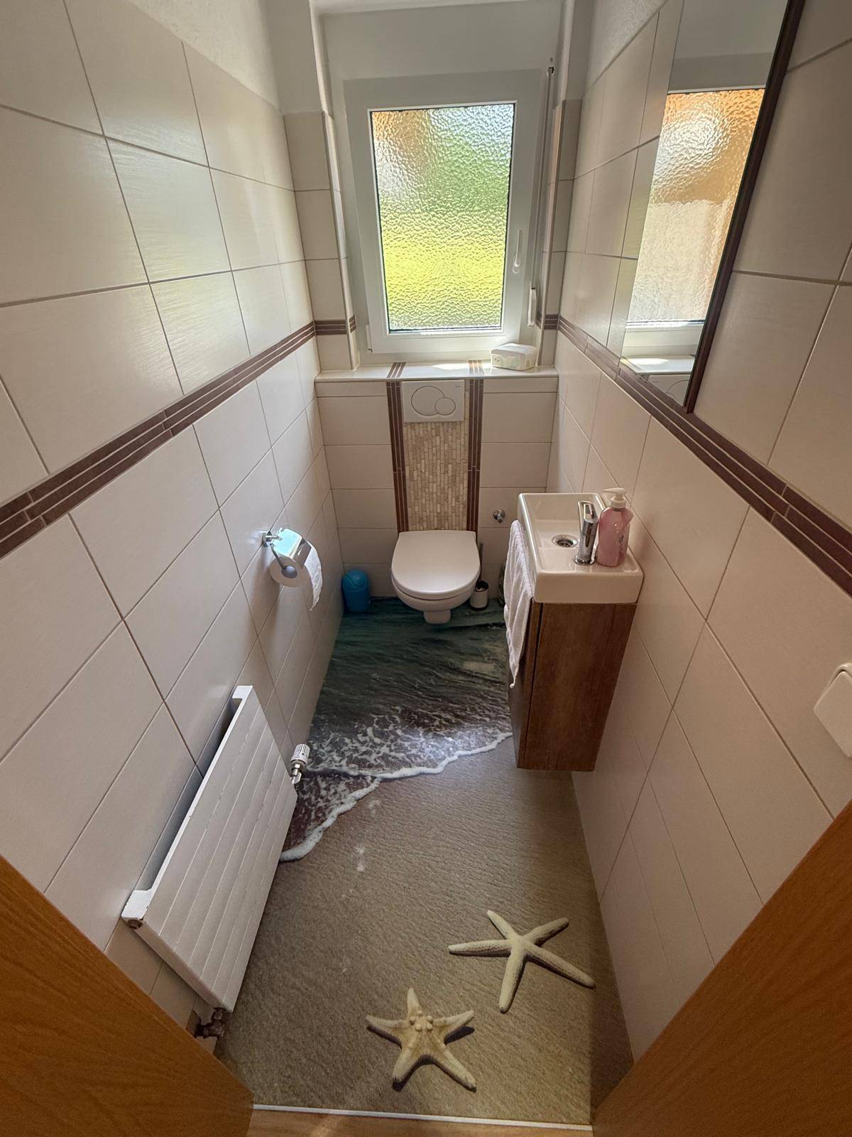 Gäste-WC mit Fenster, Wandfliesen und einem kreativen Bodenmotiv.