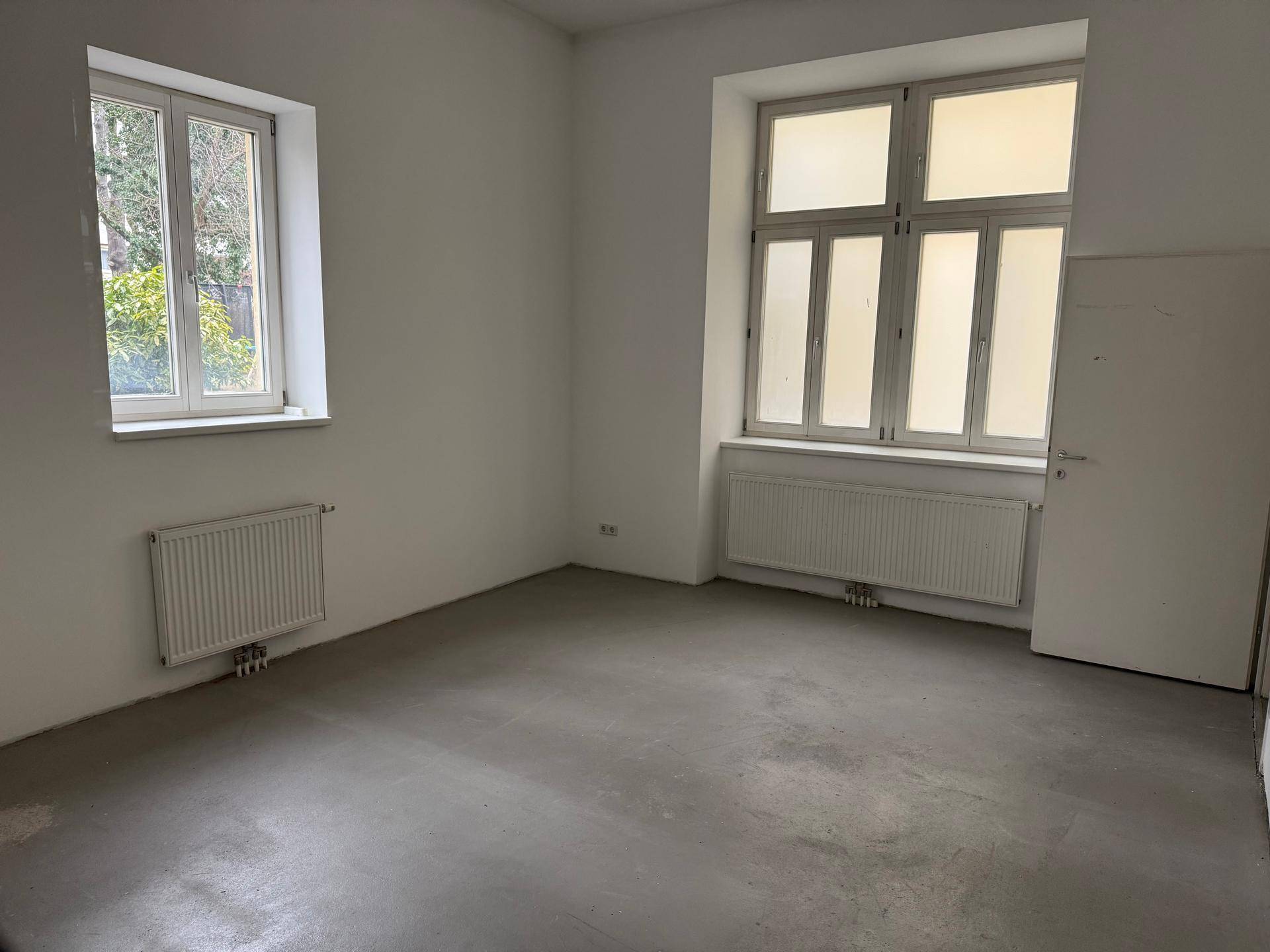 Geräumiger, leerer Raum mit zwei Fenstern und weiß gestrichenen Wänden, bereit zur individuellen Gestaltung.