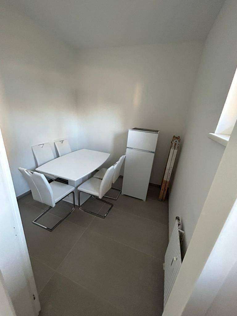 Kleiner Essbereich mit einem weißen Esstisch, passenden Stühlen und einem freistehenden Kühlschrank.