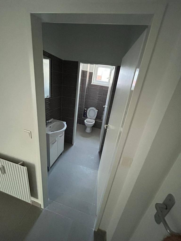 Modernes Badezimmer mit WC, Waschbecken und dunklen Fliesen an den Wänden, inklusive Fenster.