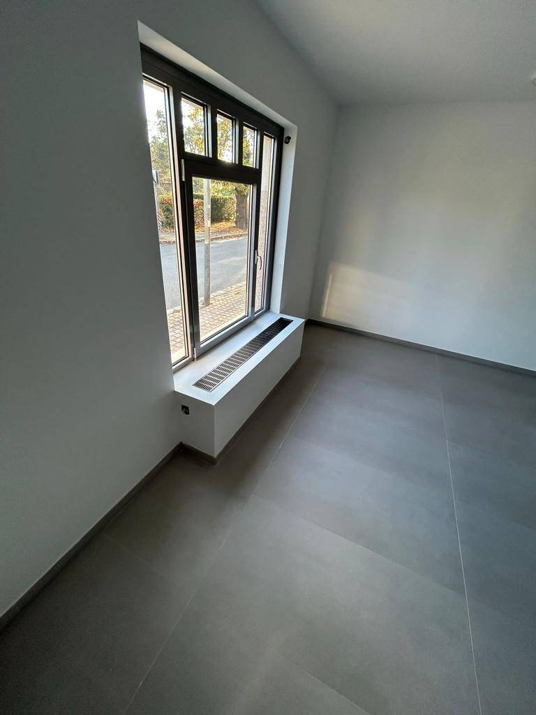 Heller Raum mit großen Fenstern, grauen Fliesen und einer Fensterbank, die als Heizkörperverkleidung dient.
