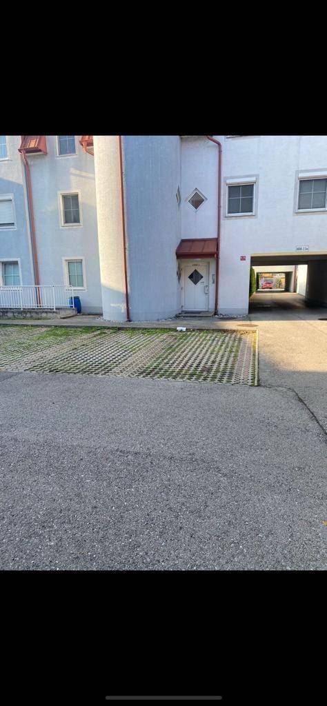 Außenansicht eines Wohngebäudes mit Parkflächen im Vordergrund und mehreren Fenstern.