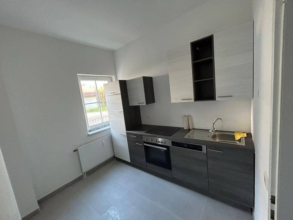Kompakte Küche mit modernen zweifarbigen Schränken, integriertem Backofen und einem Fenster für Tageslicht.