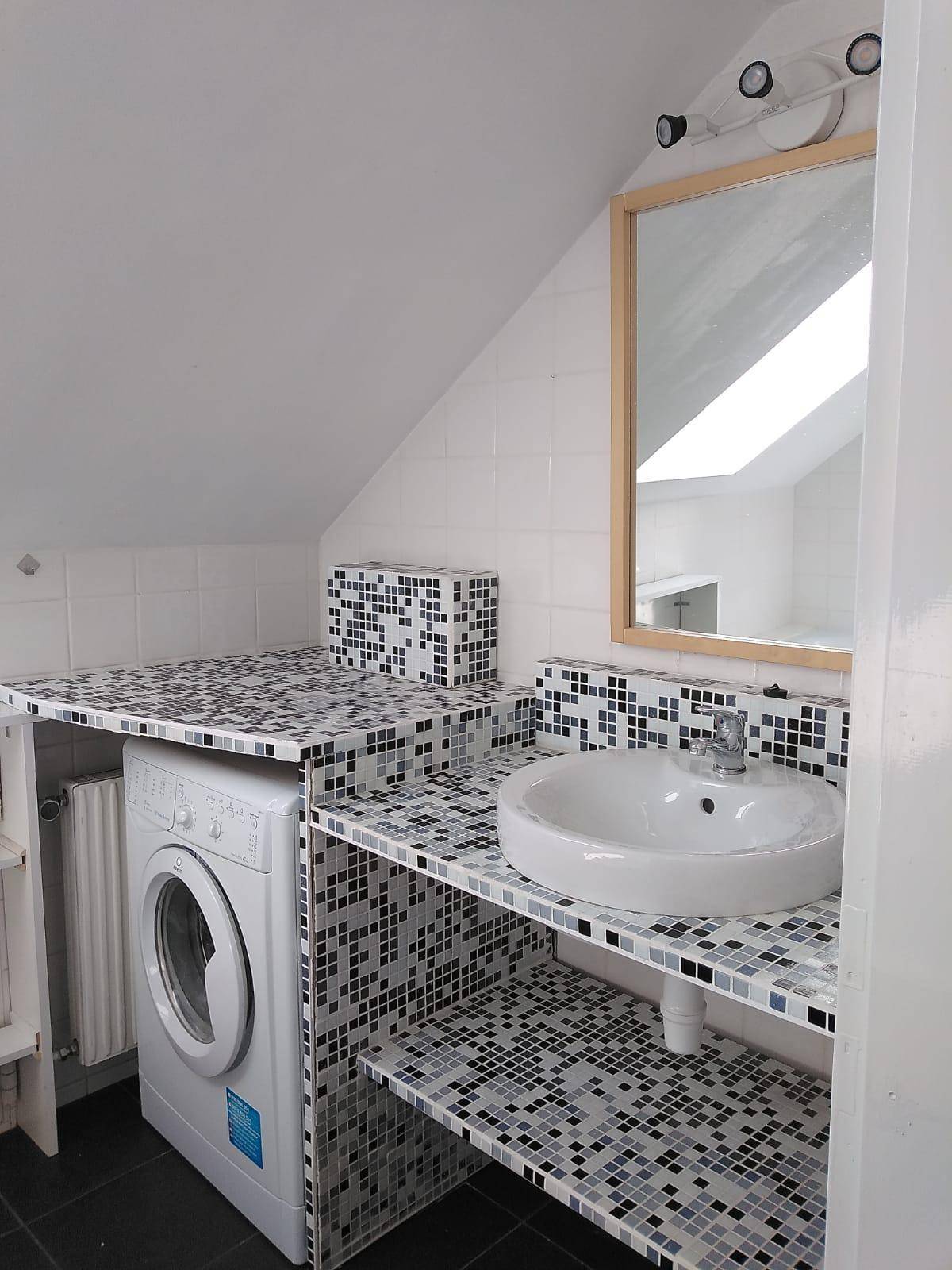 Funktionales Badezimmer mit Waschmaschine, Aufsatzwaschbecken, Spiegel und dekorativen Mosaikfliesen unter der Dachschräge.