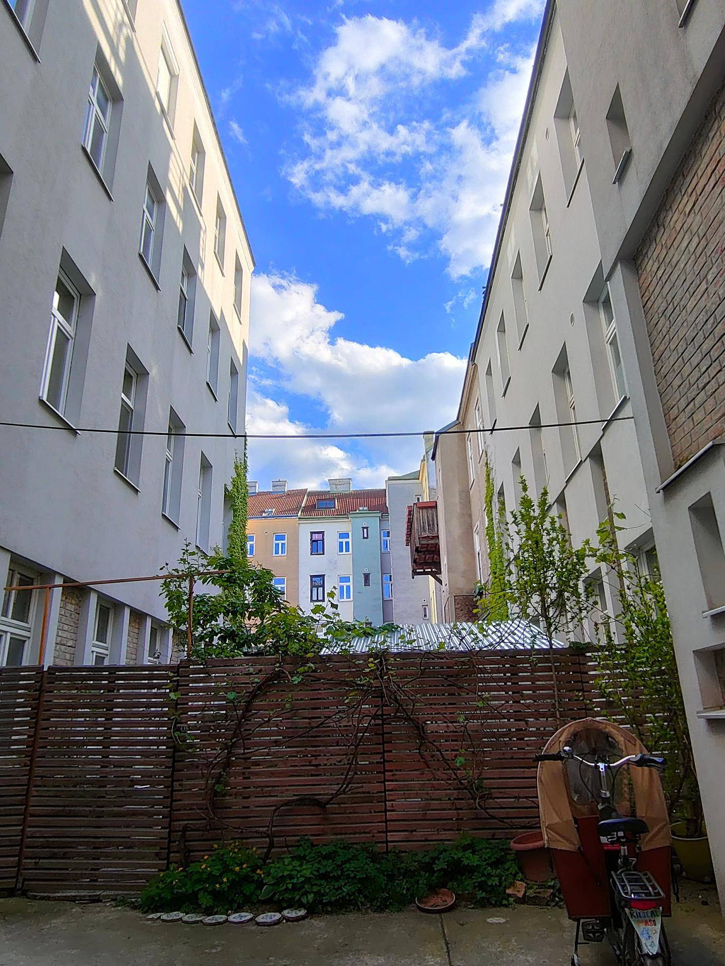 Innenhof zwischen Gebäuden mit Grünflächen, Holzzaun und einem Lastenfahrrad, das abgestellt ist.