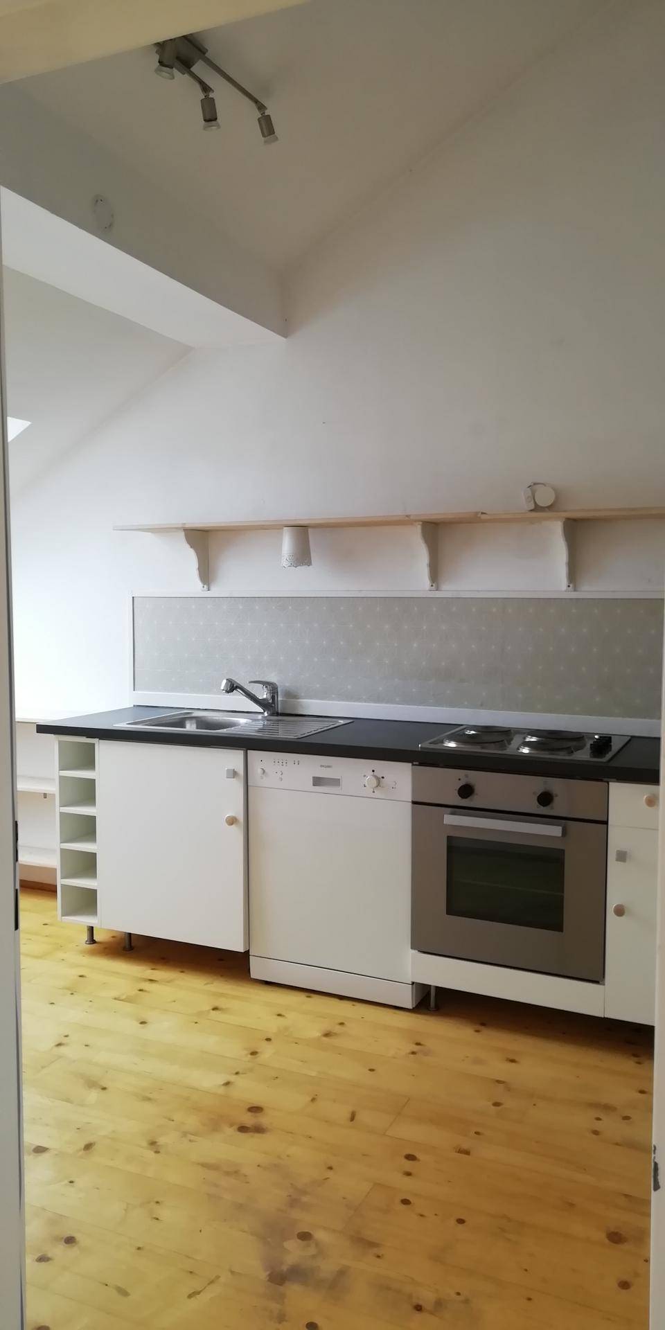 Kleine Einbauküche mit Herd, Backofen und Spülmaschine, kombiniert mit hellem Holzboden unter einer Dachschräge.