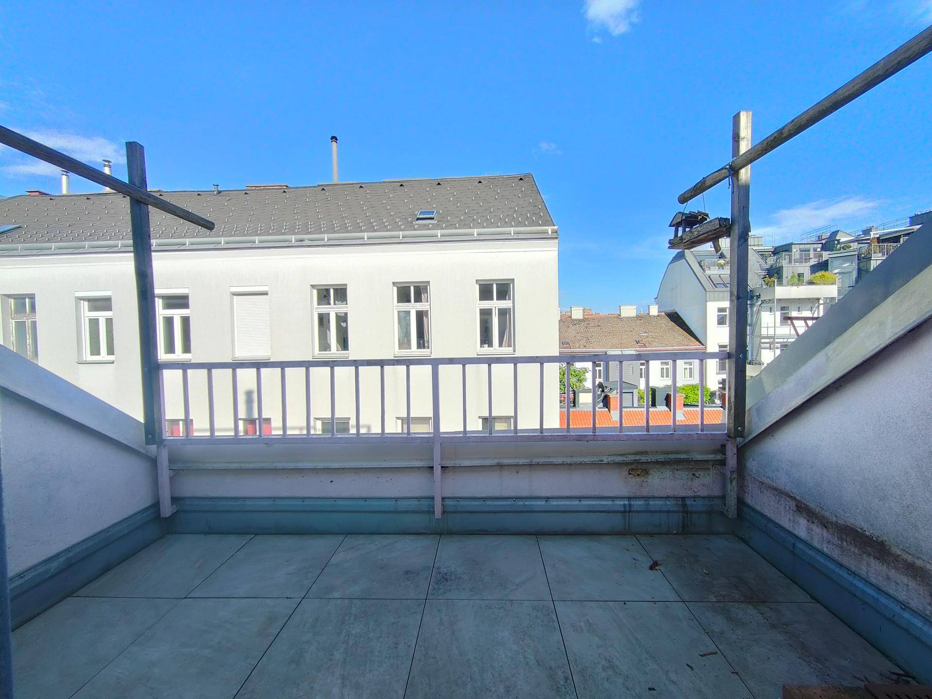 Unmöblierte Terrasse mit Blick auf umliegende Gebäude und den blauen Himmel an einem sonnigen Tag.