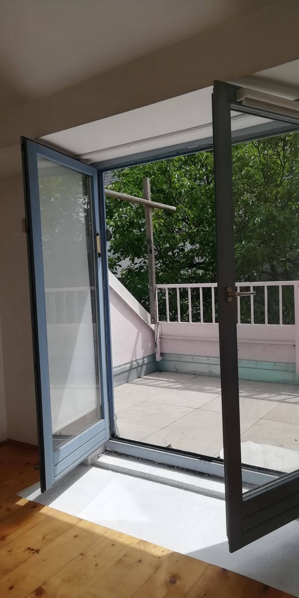 Offene Fenstertüren führen zu einem Außenbereich, mit hellem Holzboden im Innenraum und viel Tageslicht.