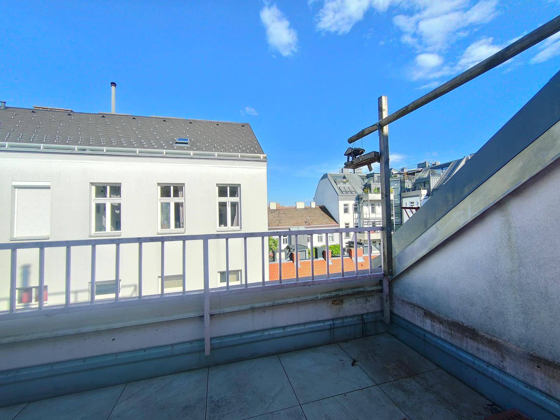 Unmöblierte Dachterrasse mit Geländer und weitem Blick auf die umliegende Stadtarchitektur unter blauem Himmel.