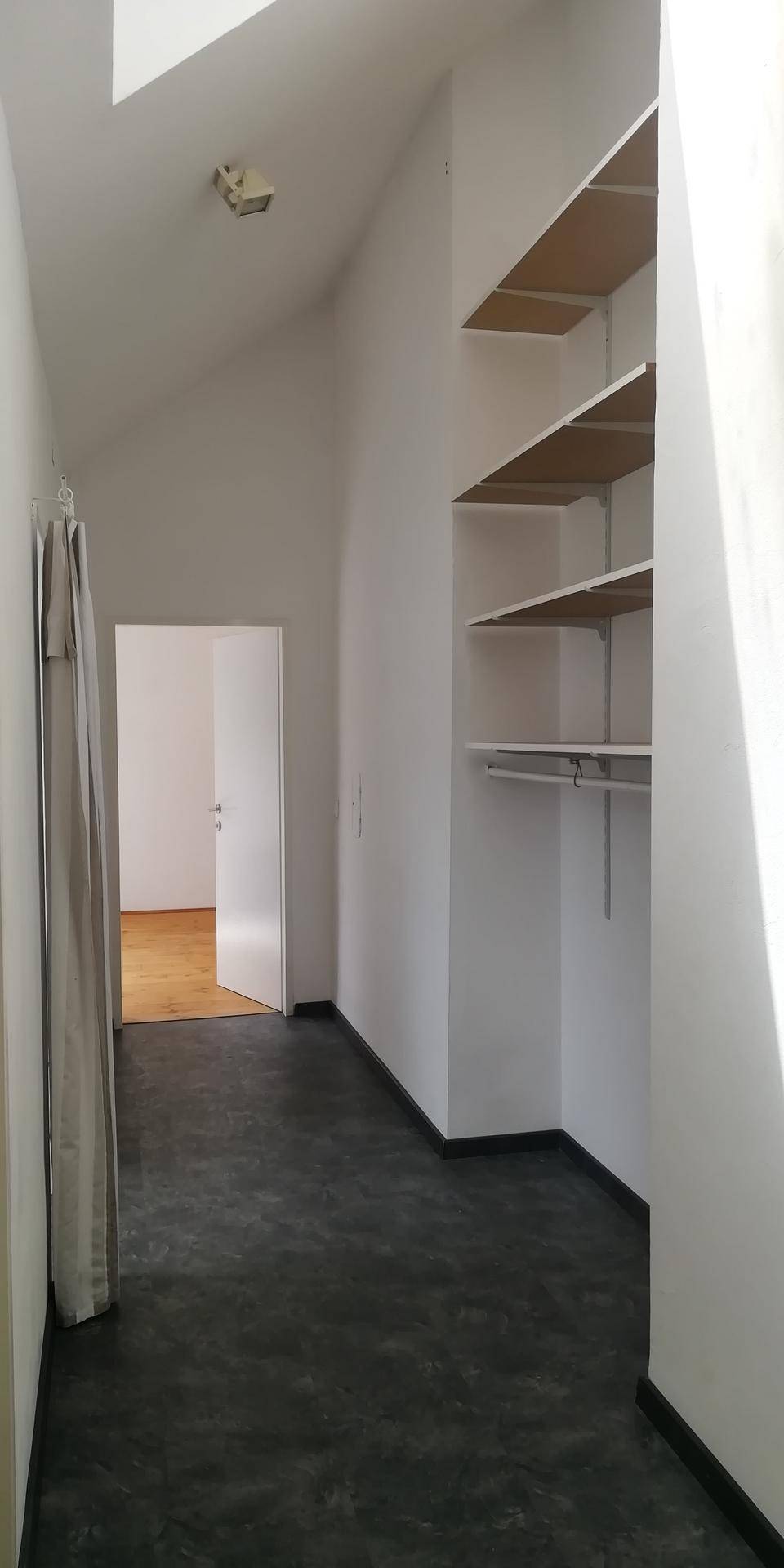 Heller Flur mit dunklem Boden, weißen Wänden und praktischen Einbauregalen unter einer schrägen Decke.