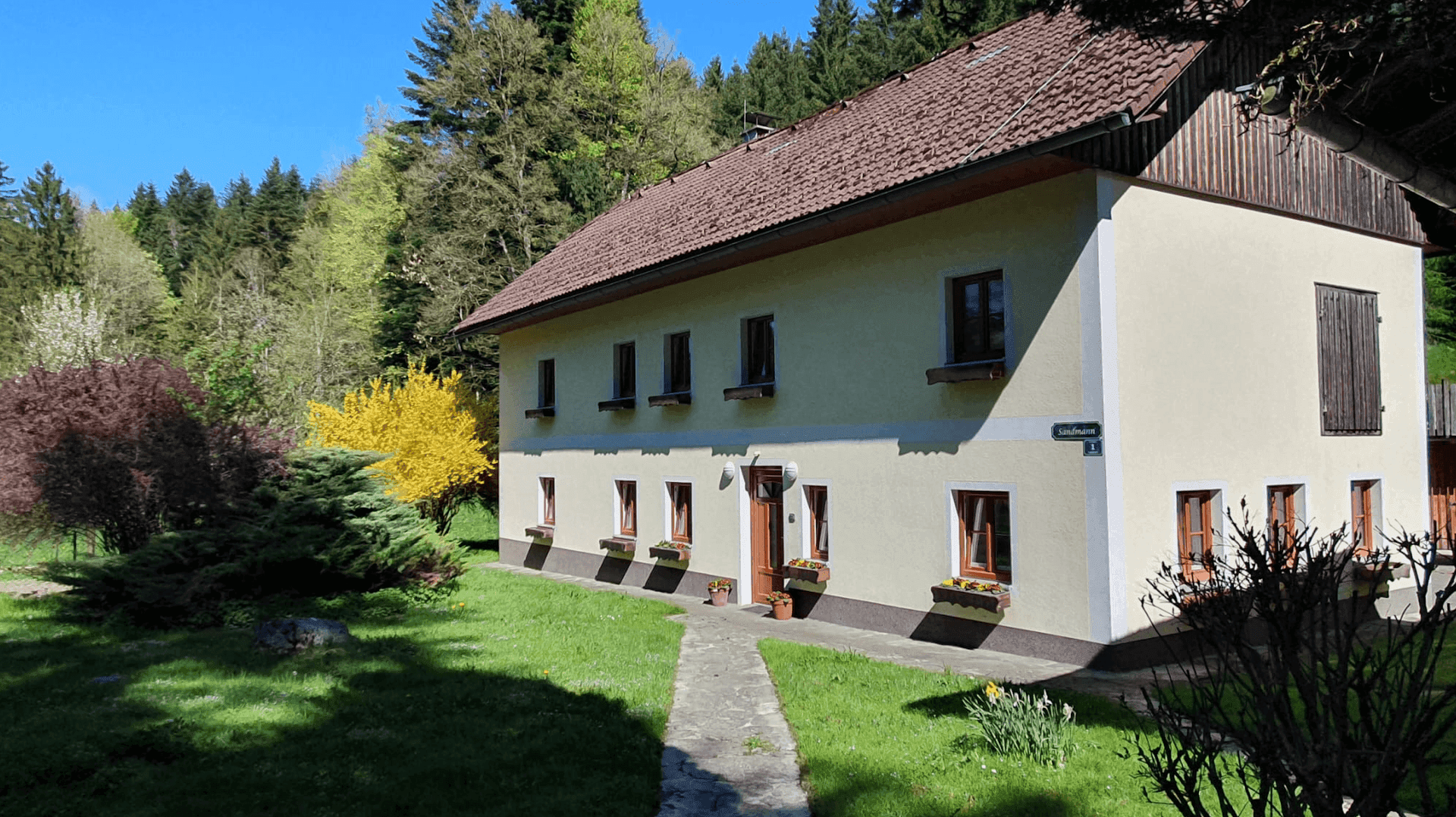 Charmantes Landhaus mit gepflegtem Garten, Steinweg und blühenden Sträuchern.