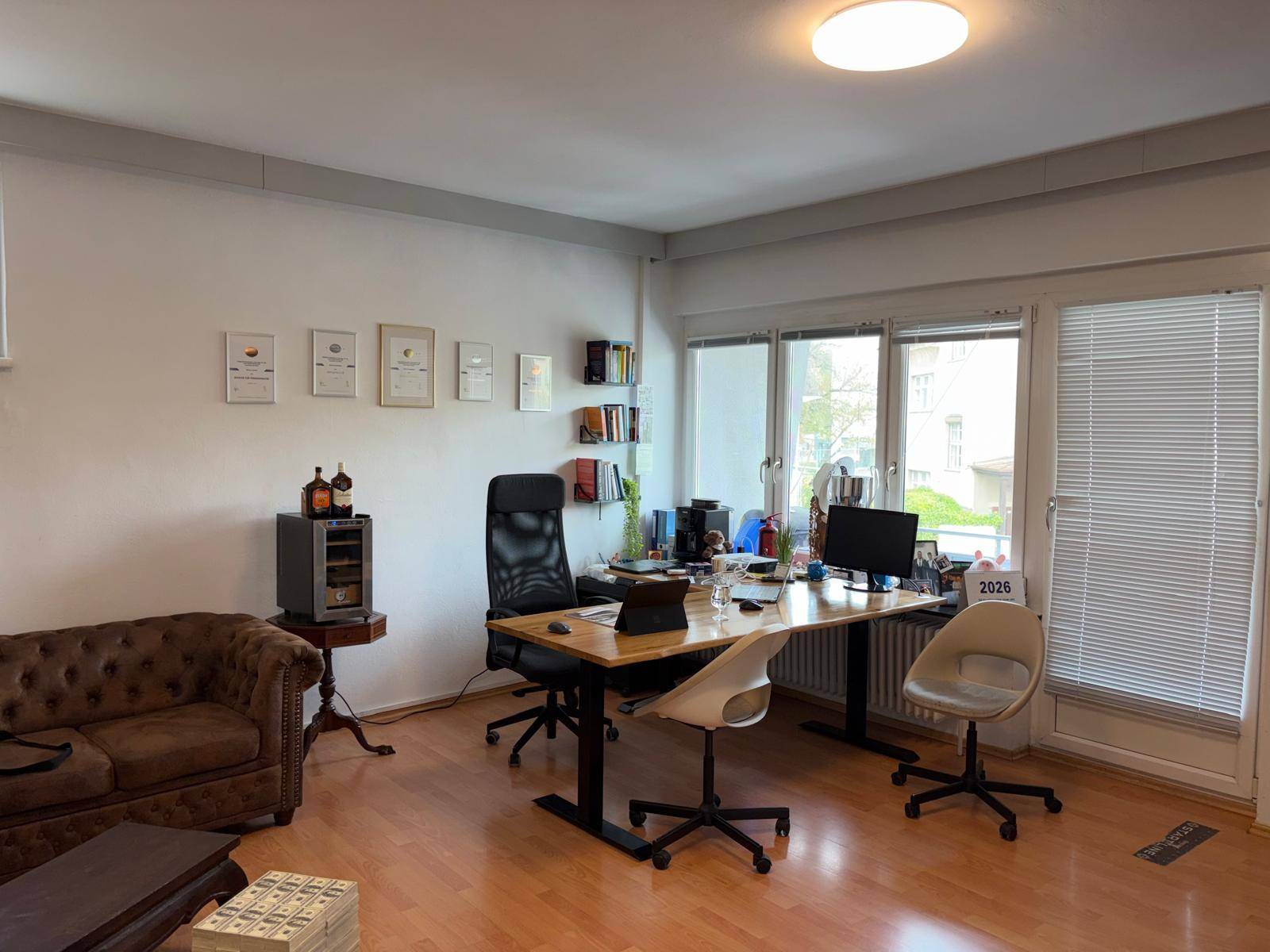 Geräumiges Büro mit großem Schreibtisch, bequemen Sofas und Blick ins Grüne durch die Fenster mit Jalousien.