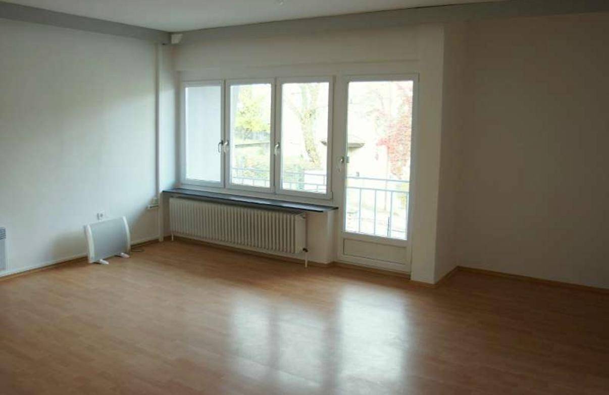 Leerer Raum mit großen Fenstern, Heizkörper und hellem Laminatboden, bereit zur individuellen Gestaltung und Nutzung.