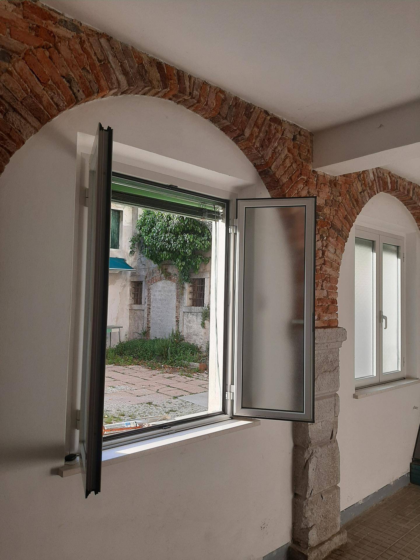 Innenraum mit freiliegenden Ziegelbögen und einem Fenster mit Blick auf einen begrünten Innenhof.