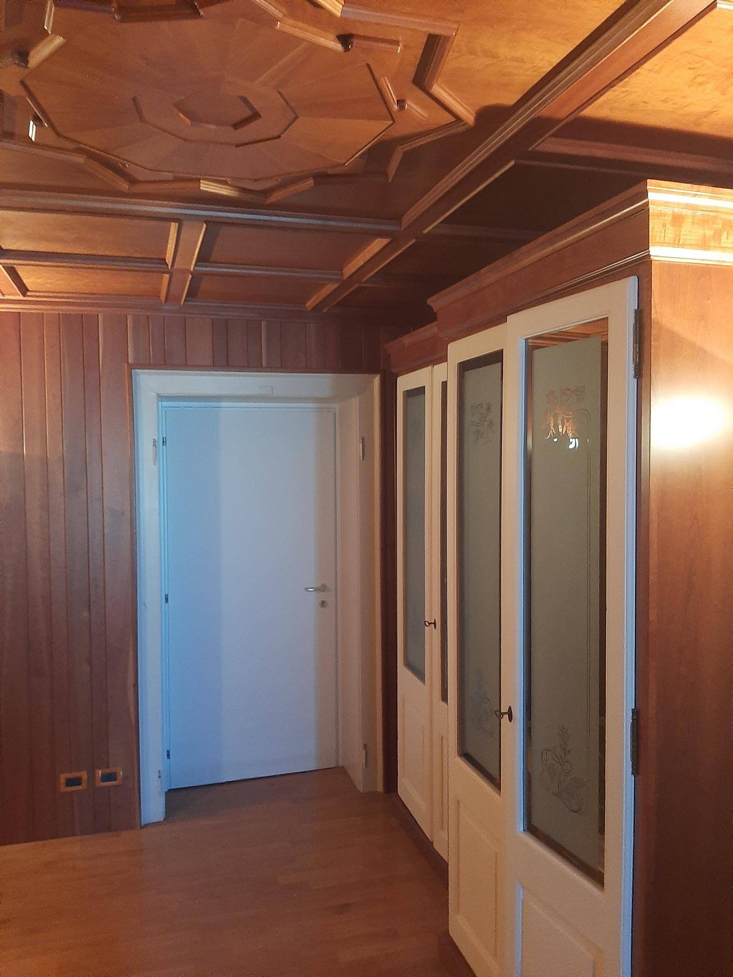 Holzvertäfelter Raum mit dekorativer Decke, einer Tür und integrierten Schränken mit Glastüren.