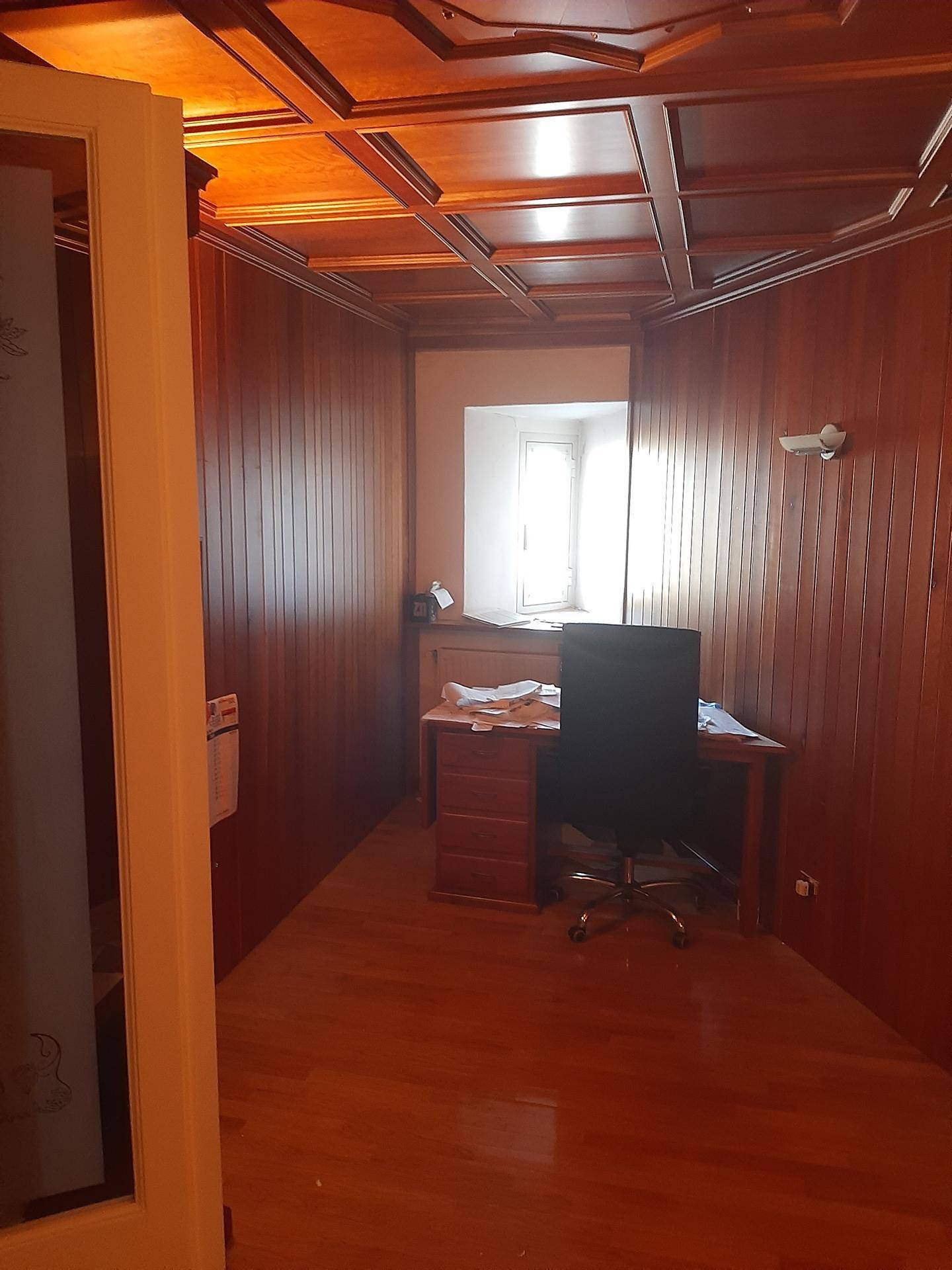 Elegantes Büro mit Holzvertäfelung, Schreibtisch und einem Fenster, das Tageslicht hereinlässt.