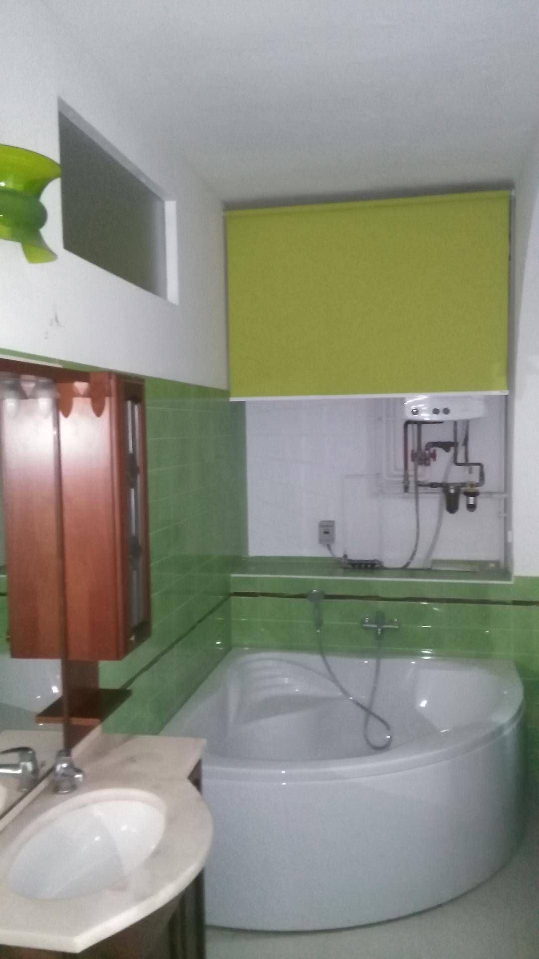 Badezimmer mit einer Eckbadewanne, grünen Fliesen und einem einzelnen Waschbecken.
