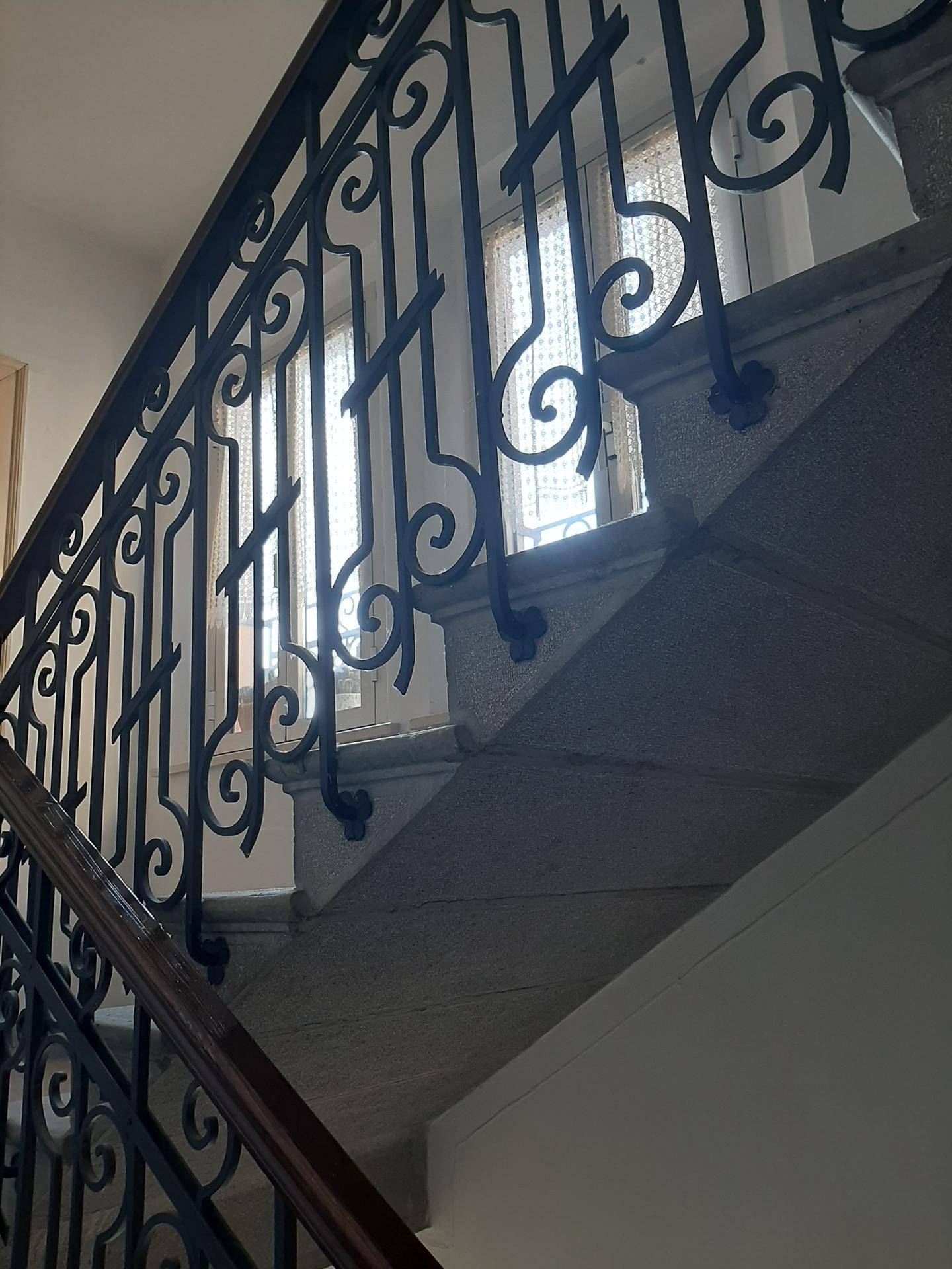 Historisches Treppenhaus mit kunstvollem schmiedeeisernem Geländer und Steinstufen.