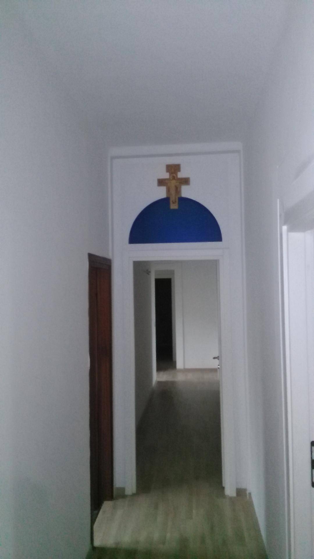 Langer Flur mit einem dekorativen blauen Bogen und einem Kreuzsymbol über dem Durchgang.