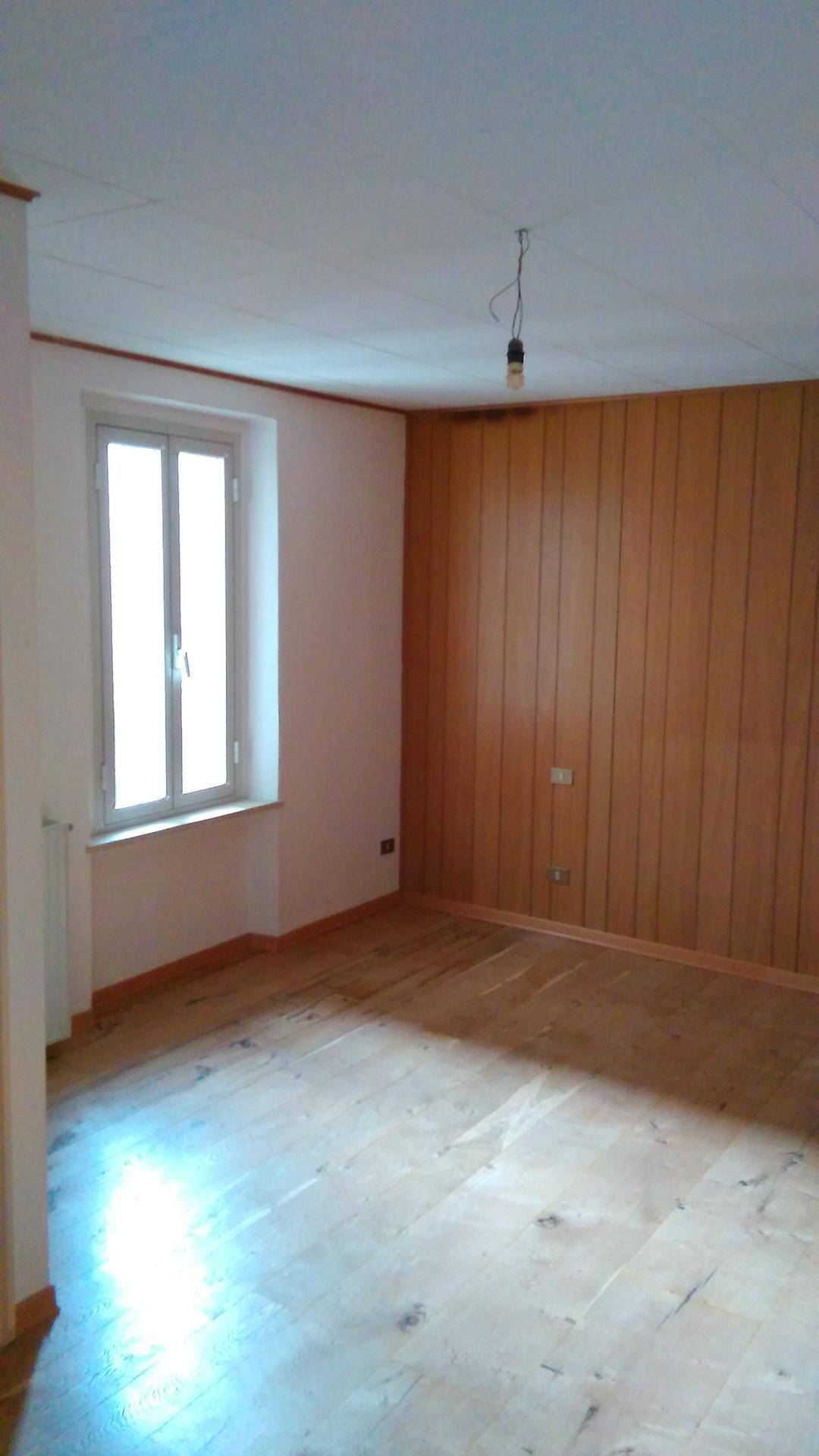 Heller Raum mit Holzboden, einer holzvertäfelten Wand und einem Fenster für natürliches Licht.