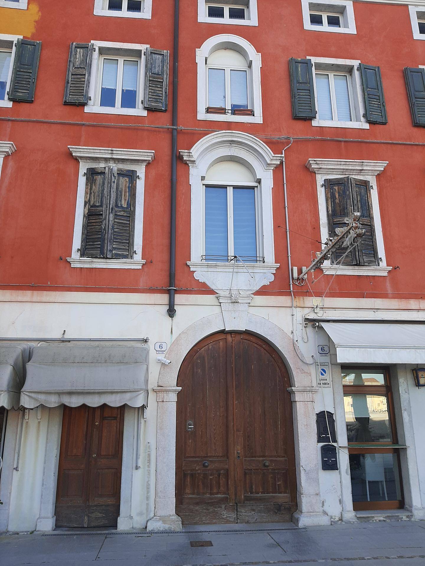 Historische rote Gebäudefassade mit einer großen, verzierten Holztür und traditionellen Fensterläden.