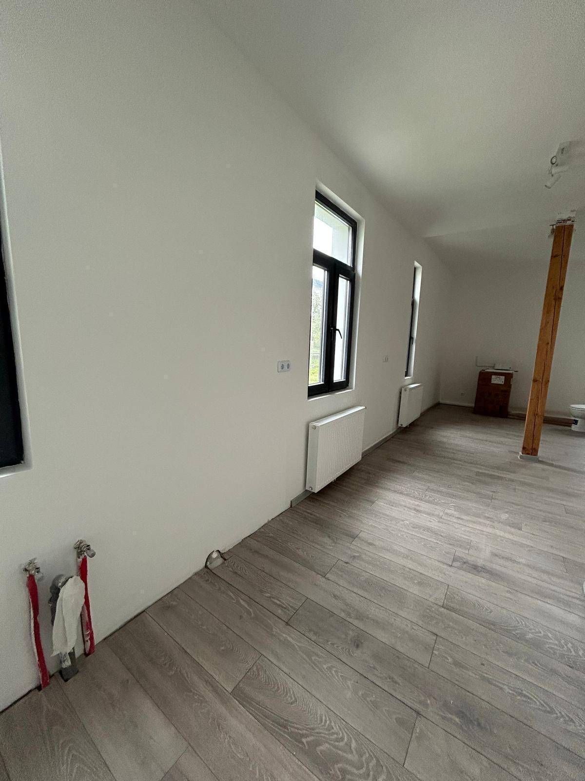 Renovierter Innenraum mit Laminatboden, großen Fenstern und Anschlüssen für Sanitärinstallationen.