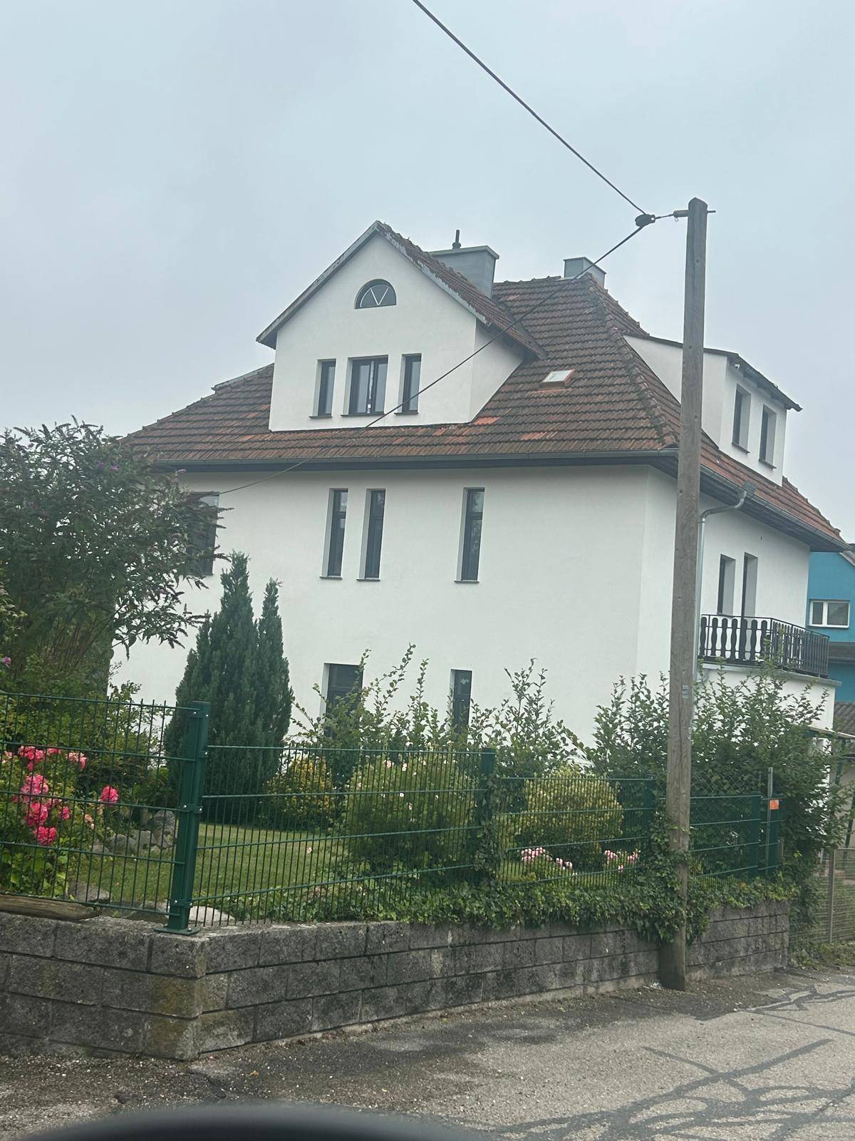 Freistehendes Wohnhaus mit weißer Fassade, Satteldach und gepflegtem Vorgartenbereich.