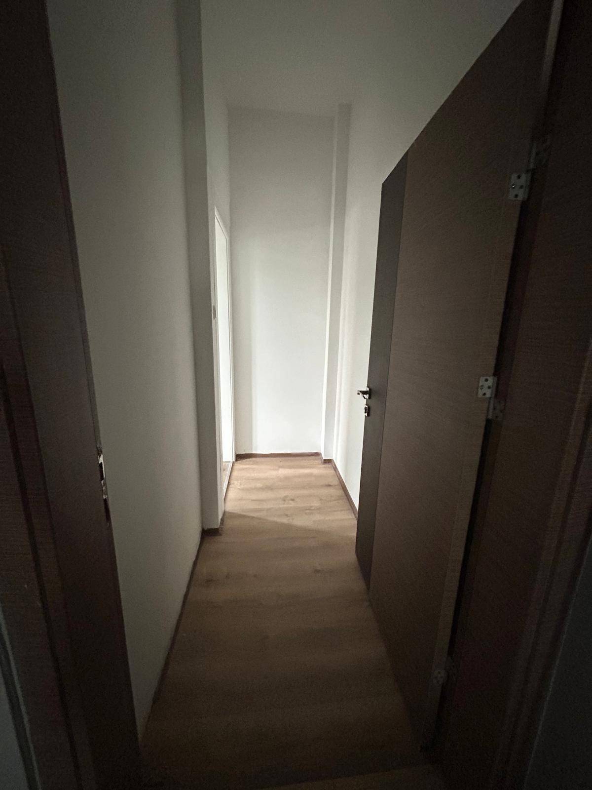 Schmaler Flur mit Holzboden und dunklen Türen, der zu weiteren Räumen führt.