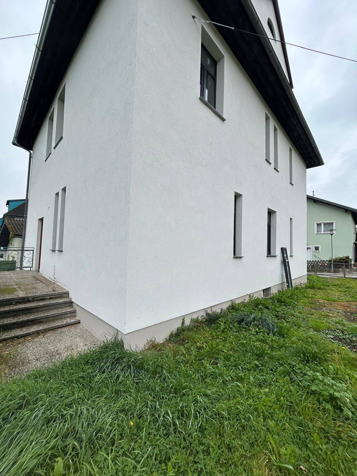 Seitenansicht des weißen Wohnhauses mit Treppenzugang und angrenzender Grünfläche.