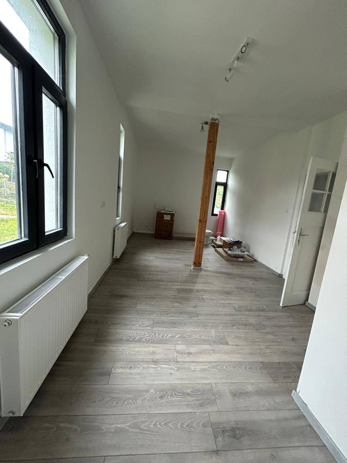Heller, leerer Raum mit neuem Laminatboden und großen Fenstern, bereit für den Ausbau.