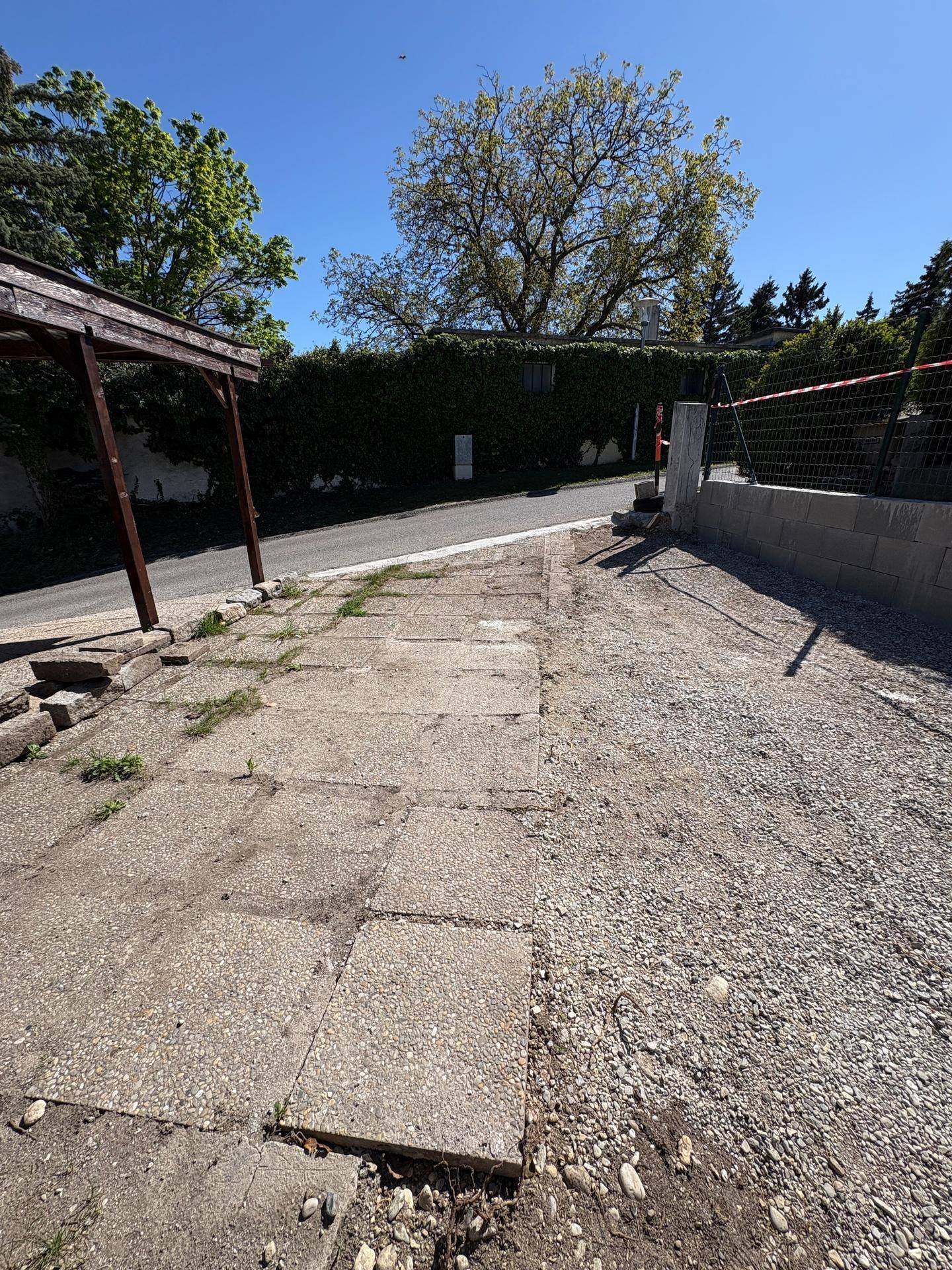 Zufahrt mit Schotter und Betonplatten, umgeben von Bäumen und einer Hecke.