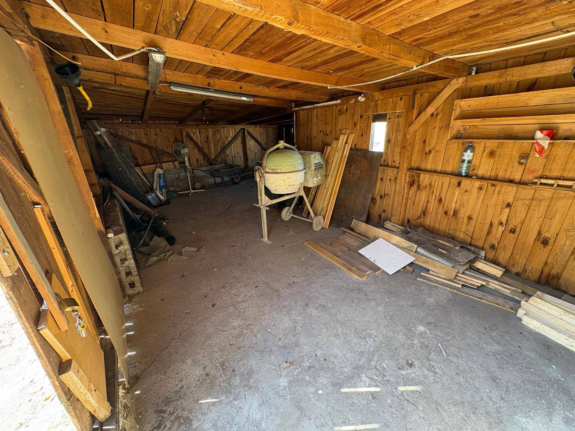 Rustikaler Innenraum einer Werkstatt mit Holzwänden, Betonboden und verschiedenen Geräten.