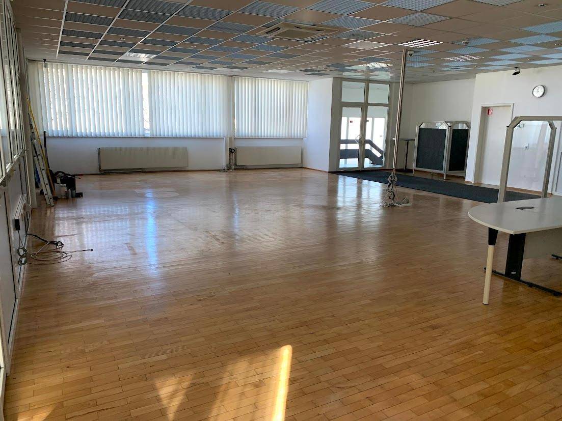Großer, heller Büroraum mit Holzparkettboden, vielen Fenstern und abgehängter Decke.