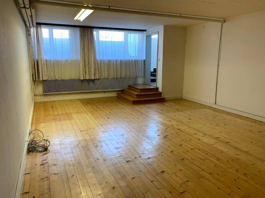 Heller Raum mit Holzplankenboden, Fenstern mit Vorhängen und einer kleinen Holztreppe zum nächsten Bereich.