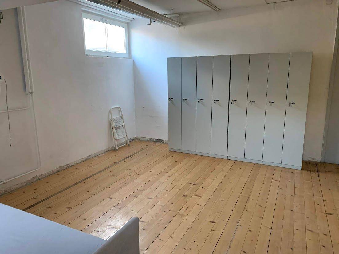 Raum mit Holzplankenboden, weißen Wänden und einer Reihe grauer Spinde, ideal als Lager oder Umkleide.