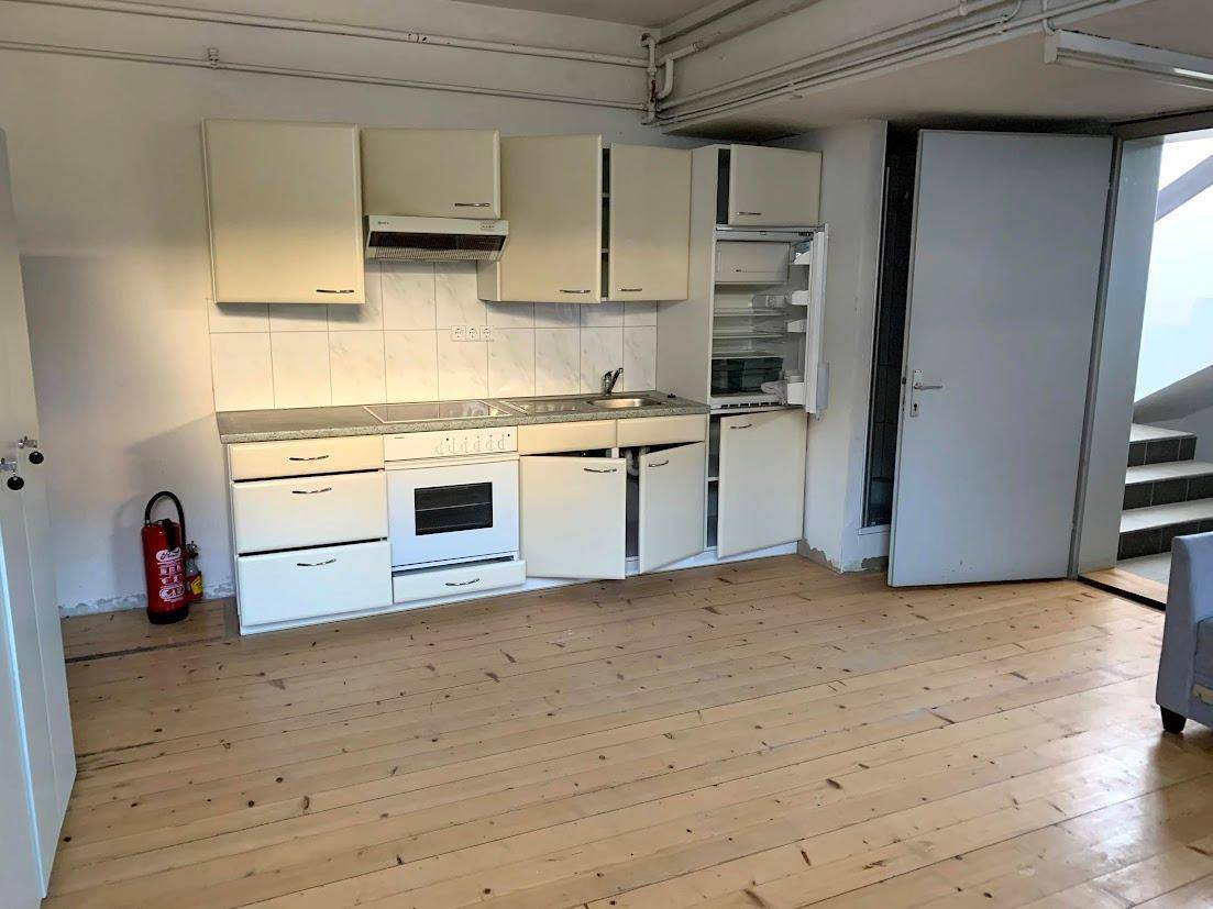Geräumige Küchenzeile mit Holzplankenboden, Herd, Kühlschrank und Treppenaufgang, ideal für Mitarbeiter.