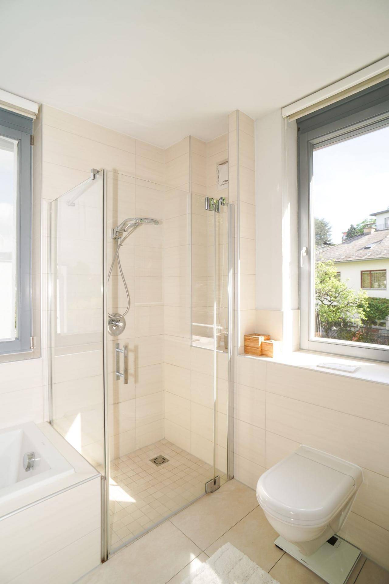 Helles Badezimmer mit Dusche, WC und Fenster, das viel Tageslicht hereinlässt.