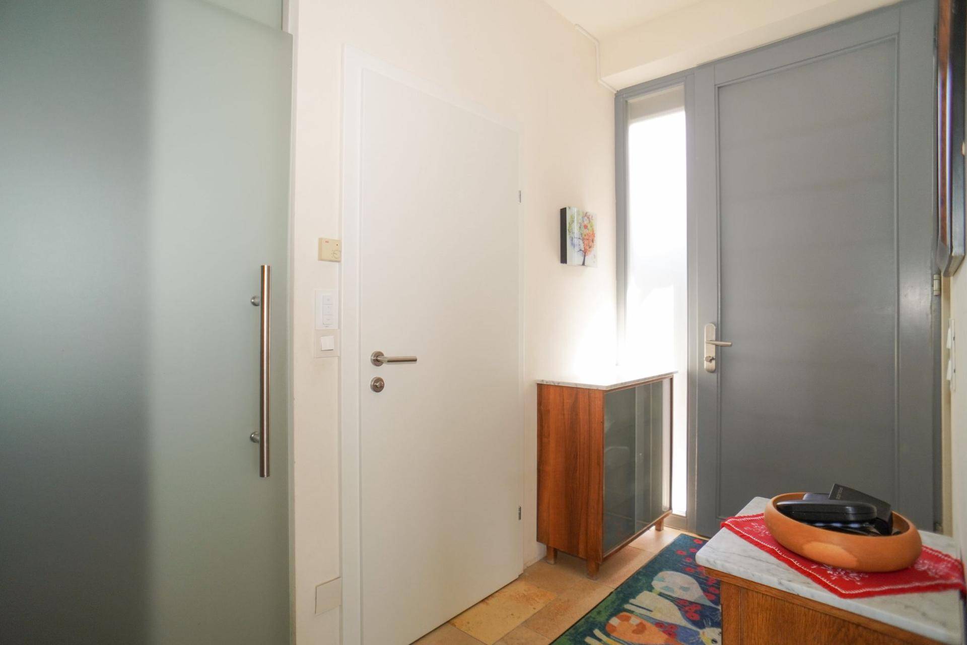 Eingangsbereich mit heller Tür, Fenster und Fliesenboden, der in den Wohnbereich führt.