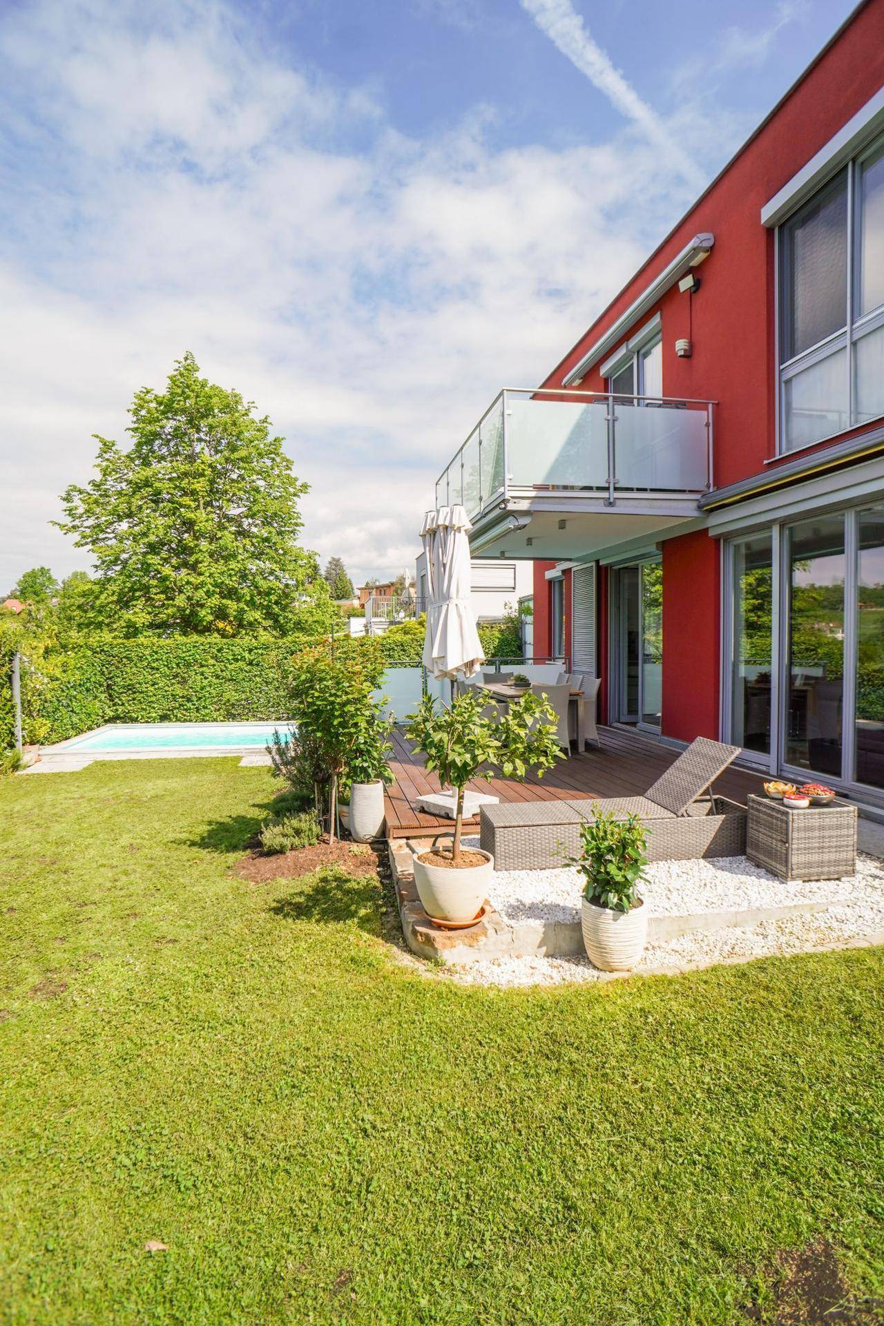 Gepflegter Garten mit Rasenfläche und einer Holzterrasse am modernen Haus.