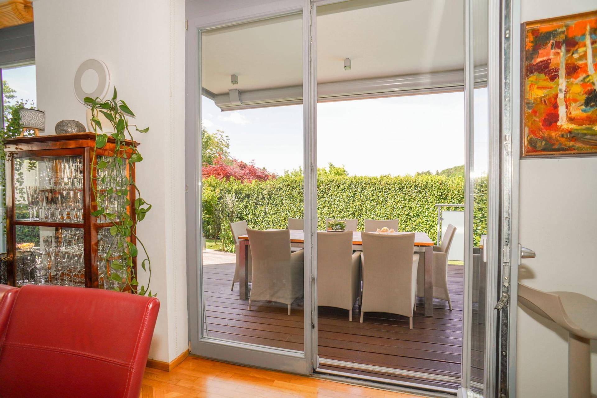 Große Glasschiebetür öffnet den Wohnbereich zur möblierten Holzterrasse mit Gartenblick.