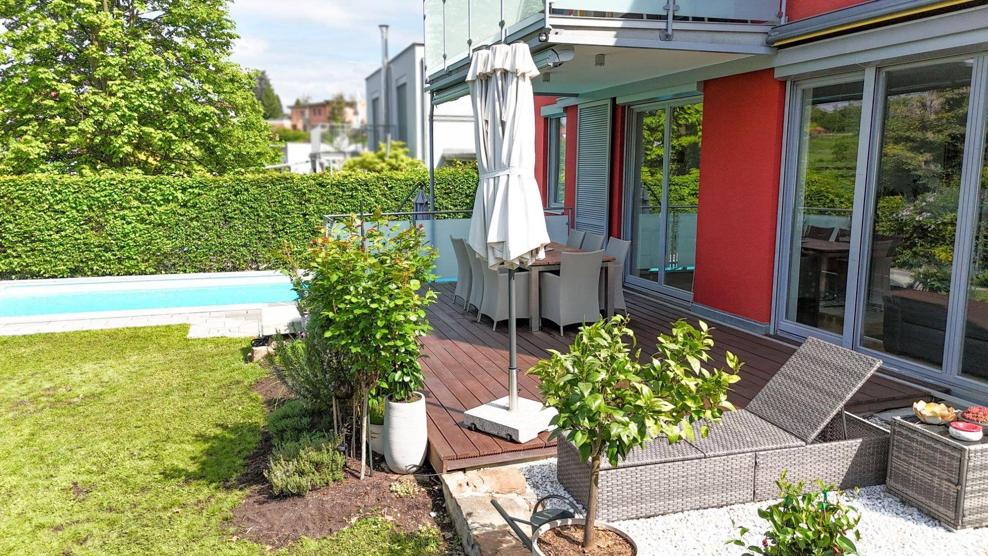Gemütliche Holzterrasse mit Gartenmöbeln, Sonnenschirm und Blick ins Grüne.