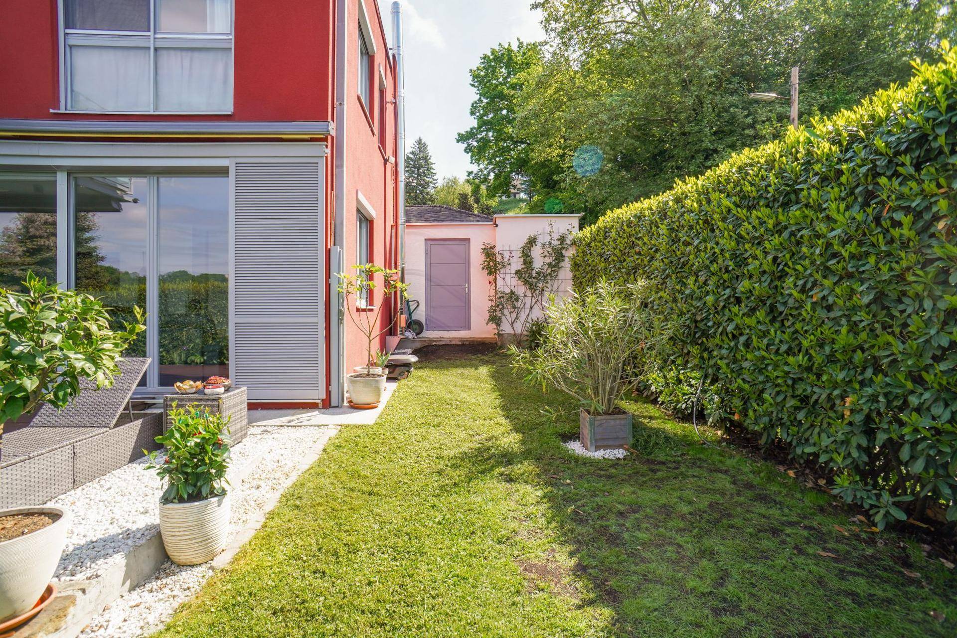 Langer Gartenbereich mit Rasen, Hecke und einem kleinen Gartenhaus im Hintergrund.