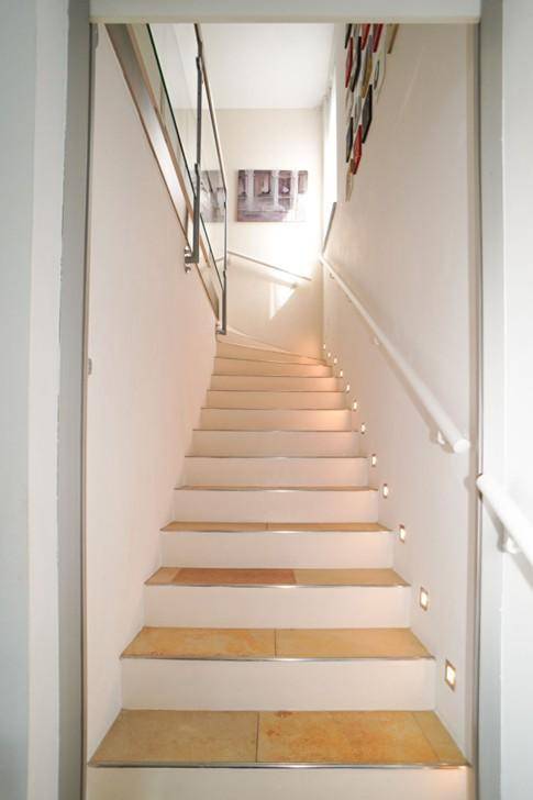 Helle Treppe mit Stufenbeleuchtung und modernem Geländer führt in die obere Etage.