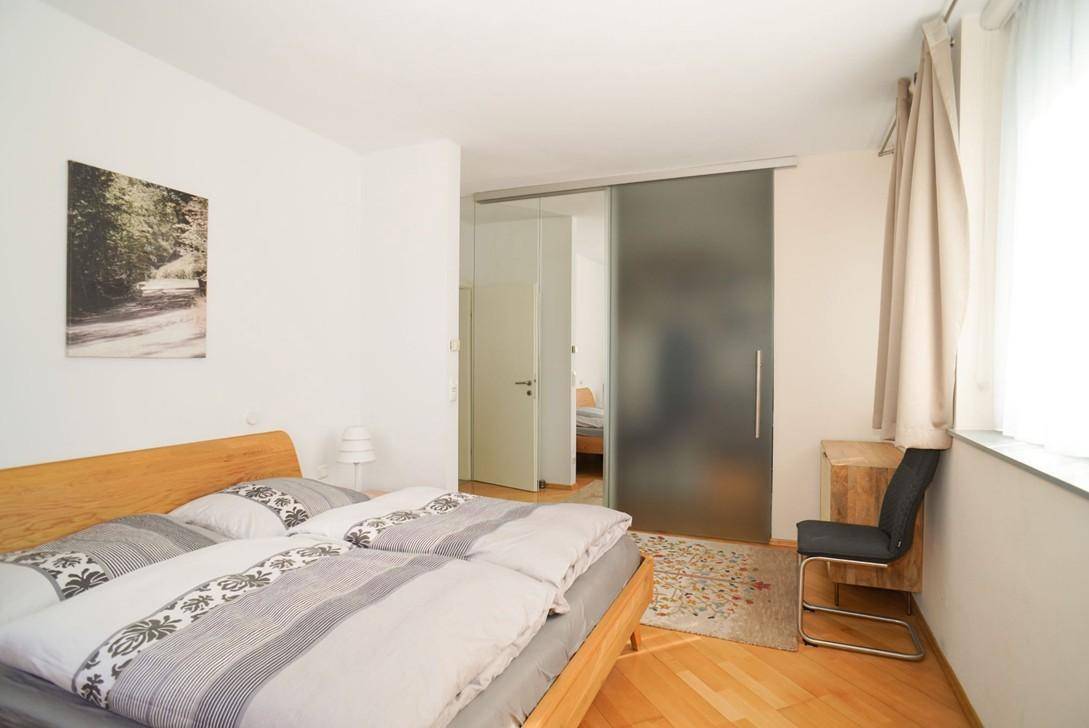 Schlafzimmer mit Holzbett und Schiebetür, die zu einem begehbaren Kleiderschrank führt.