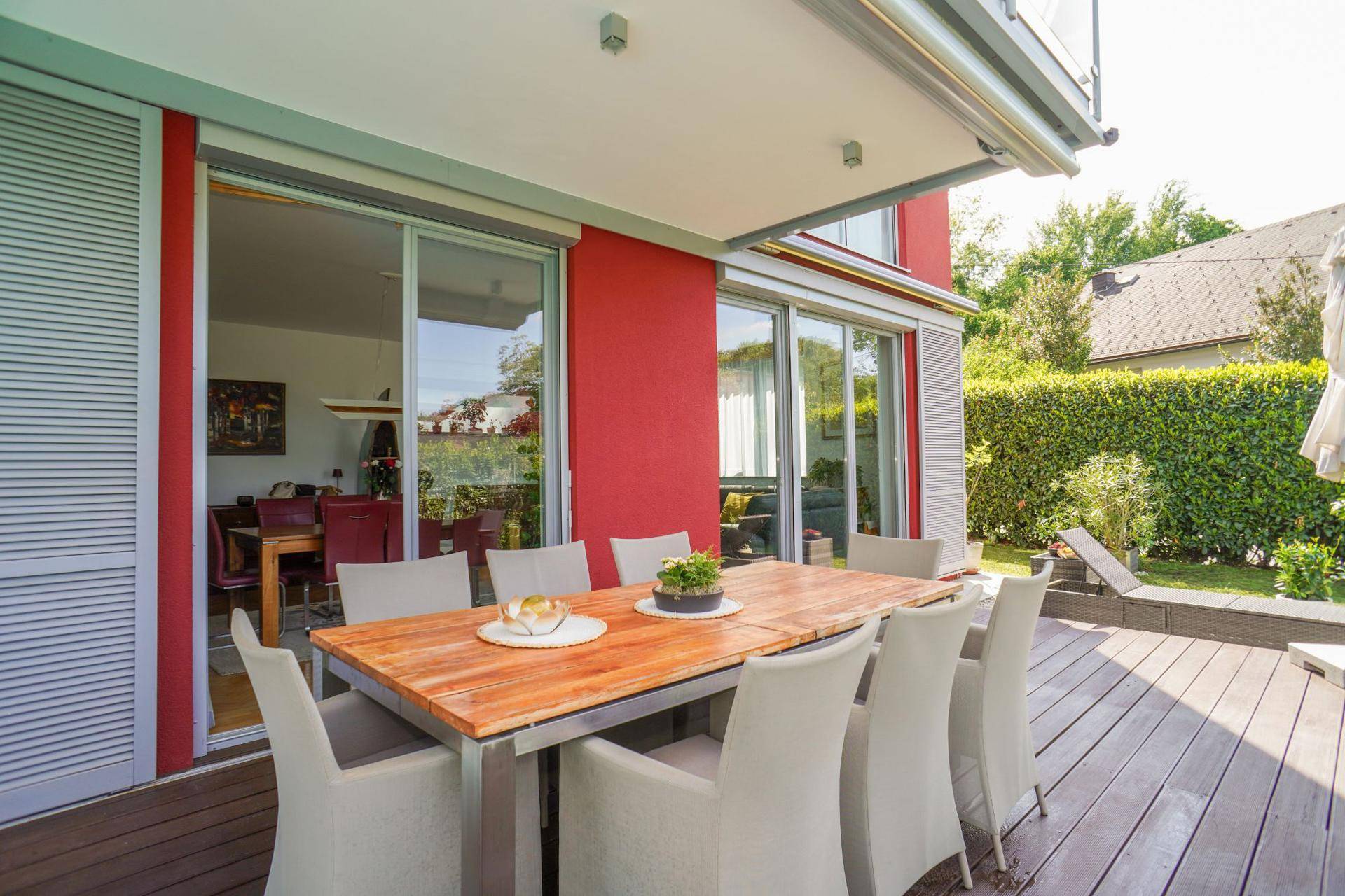 Geräumige Holzterrasse mit Esstisch und Blick auf den Garten, direkt vom Wohnbereich zugänglich.